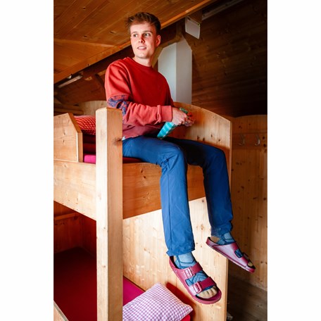 Mann sitzt auf Hochbett im Hüttenlager 