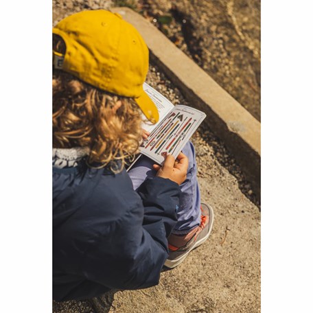 Kind mit gelben Cap blättert sitzend durch Kinder Bergpass