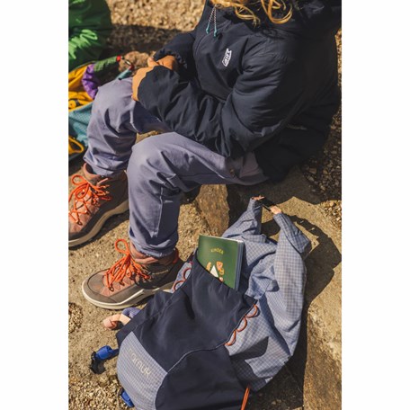 Kind sitzt neben Rucksack, aus dem Bergpass lugt