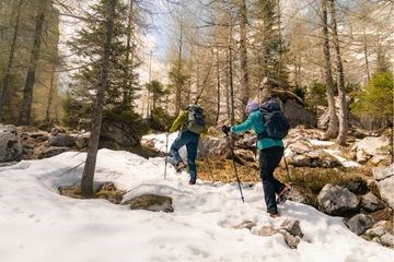 Zwei Personen queren ein Schneehang umgeben von felsigem Gelände am Berg