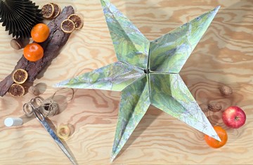 auf einem weihnachtlich dekorierten Holztisch liegt ein Papierstern 